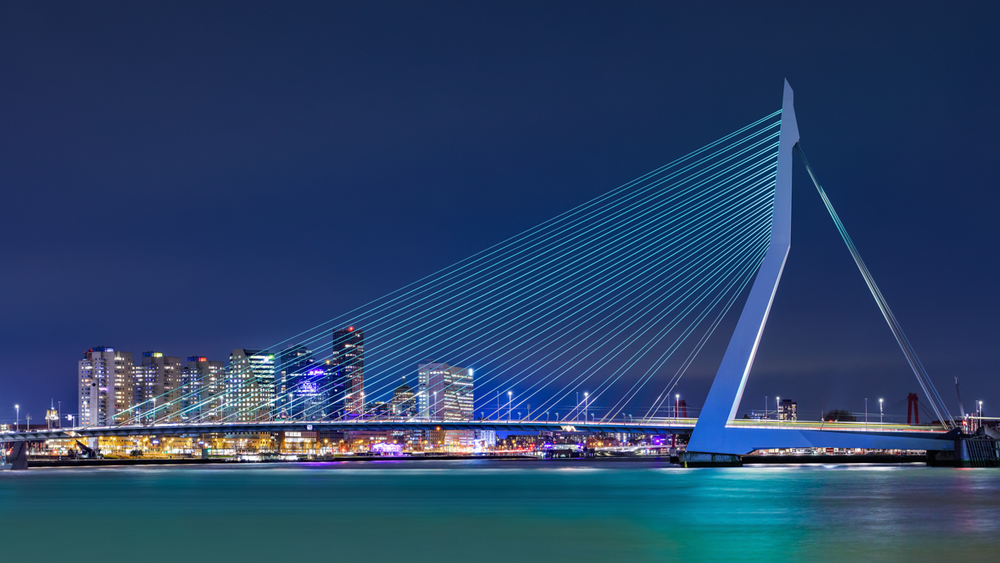 Cityscape met een verlichte Erasmusbrug tegen een strak blauwe Rotterdamse lucht. 