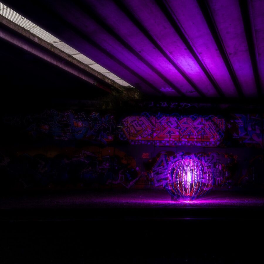 Wat een krachtige en originele inzending voor het thema Buitenkunst! Deze foto vangt perfect de ontmoeting tussen twee werelden: de tijdelijke, etherische lichtkunst in de vorm van een ‘orb’ en de permanente, rauwe expressie van graffiti. De tunnel onder de snelweg vormt een spannend decor dat zowel afschrikt als intrigeert. De paarse gloed brengt een bijna magische sfeer in een verder industriële omgeving. Het lijnenspel van het plafond versterkt de compositie en trekt je blik direct naar het lichtobject. Een mooie interpretatie van buitenkunst – gewaagd, creatief en met oog voor contrast. Goed gezien én goed uitgevoerd!