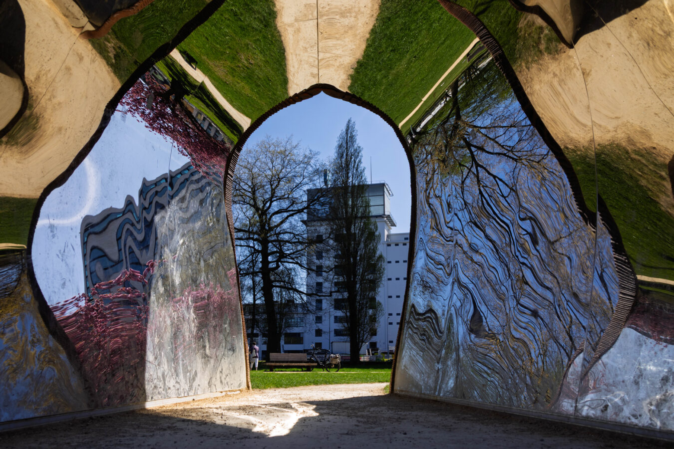FOTOGRAFIE Helma Lomans - Helma, wat een fascinerend beeld heb je hier neergezet! Je hebt een kunstwerk gekozen dat niet alleen visueel prikkelt, maar ook letterlijk de werkelijkheid vervormt. De spiegelende, golvende wanden creëren een bijna surrealistisch doorkijkje naar de buitenwereld, waarin natuur en architectuur samensmelten tot een nieuwe compositie. De keuze voor dit standpunt kijkend door de opening laat ons even meereizen in jouw verwondering. Een sterk voorbeeld van hoe buitenkunst niet alleen aanwezig is, maar ook de manier waarop we de wereld zien, compleet kan veranderen. Prachtige blik, Helma!